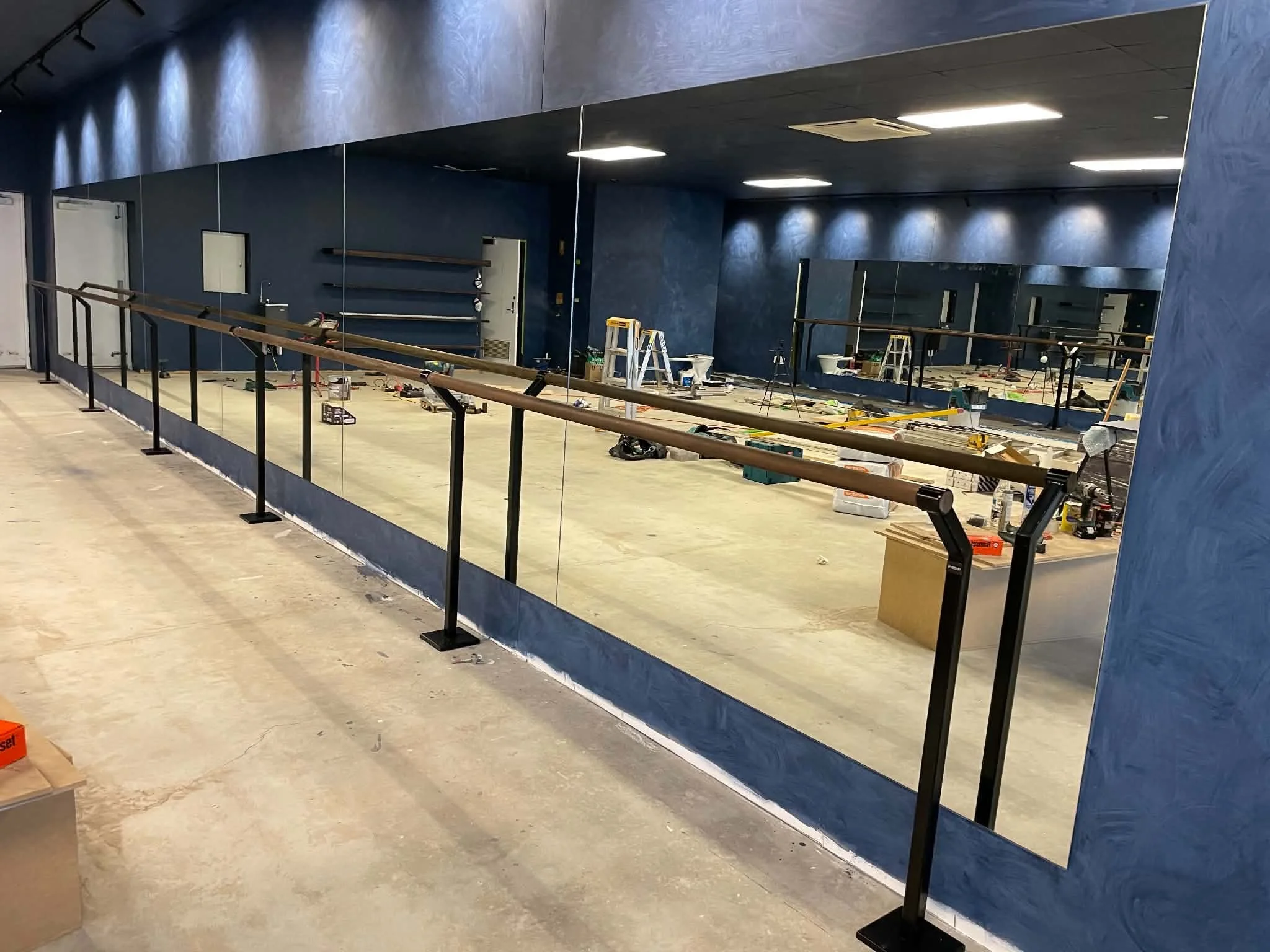 Interior of a room under renovation with a large mirror on the wall, construction tools and supplies scattered on the floor, and protective temporary barriers.