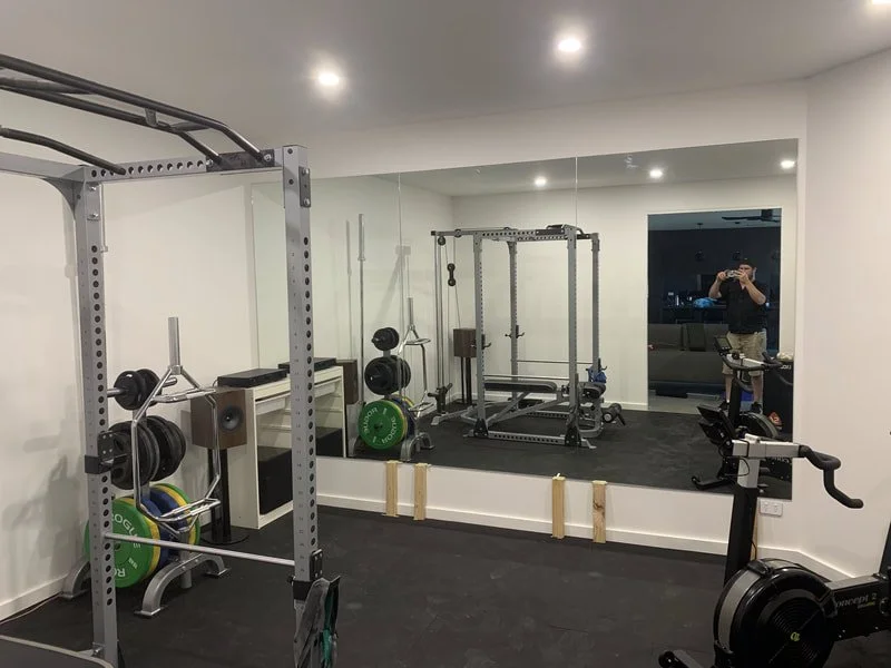 Home gym with various workout equipment, including a squat rack, weight plates, a rowing machine, and a mirrored wall.