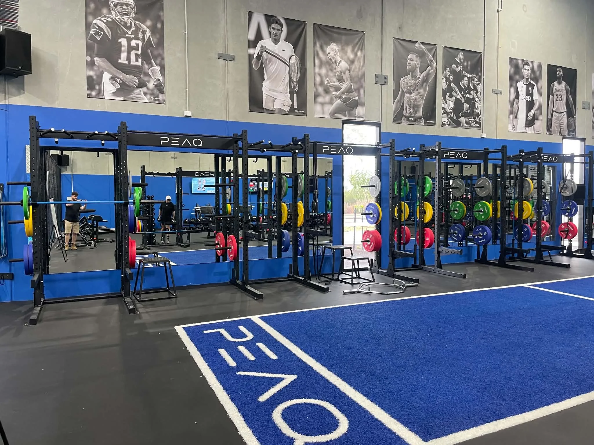 Interior of a gym with black weight racks, colorful weight plates, and large black-and-white posters of athletes on the wall.