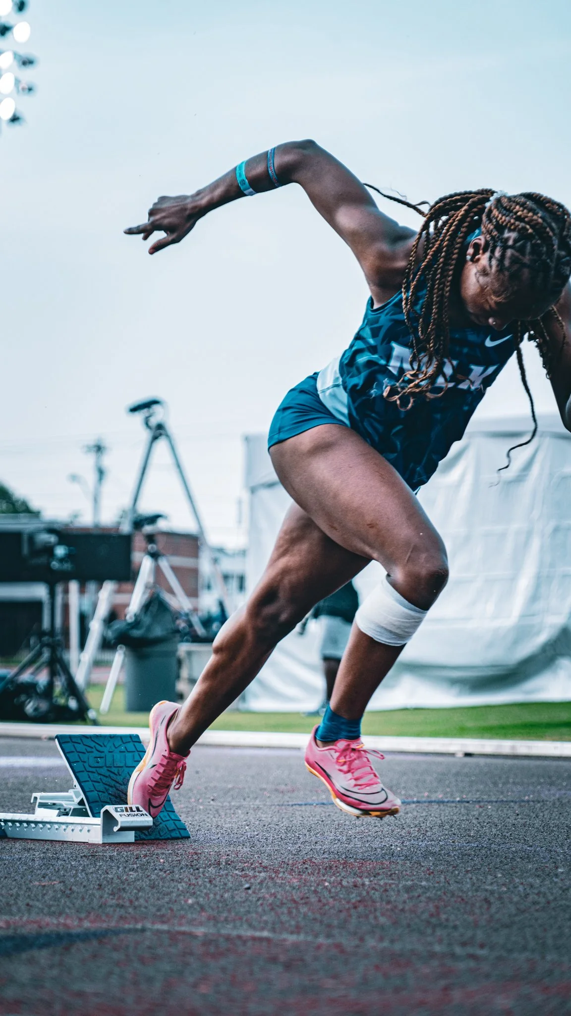 Female athlete in athletic gear starting a race on a track with a starting block.