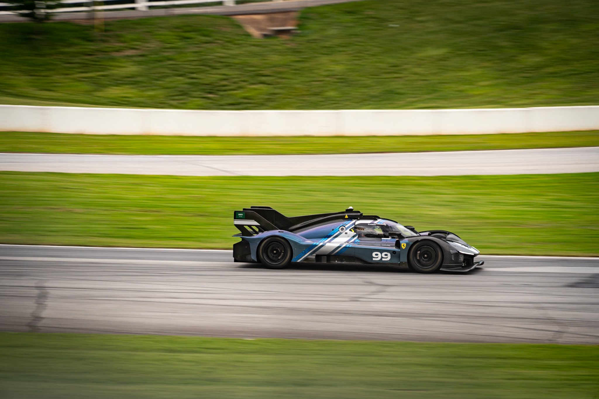 Race car on track with green grassy background, car has the number 99 and a sleek black design