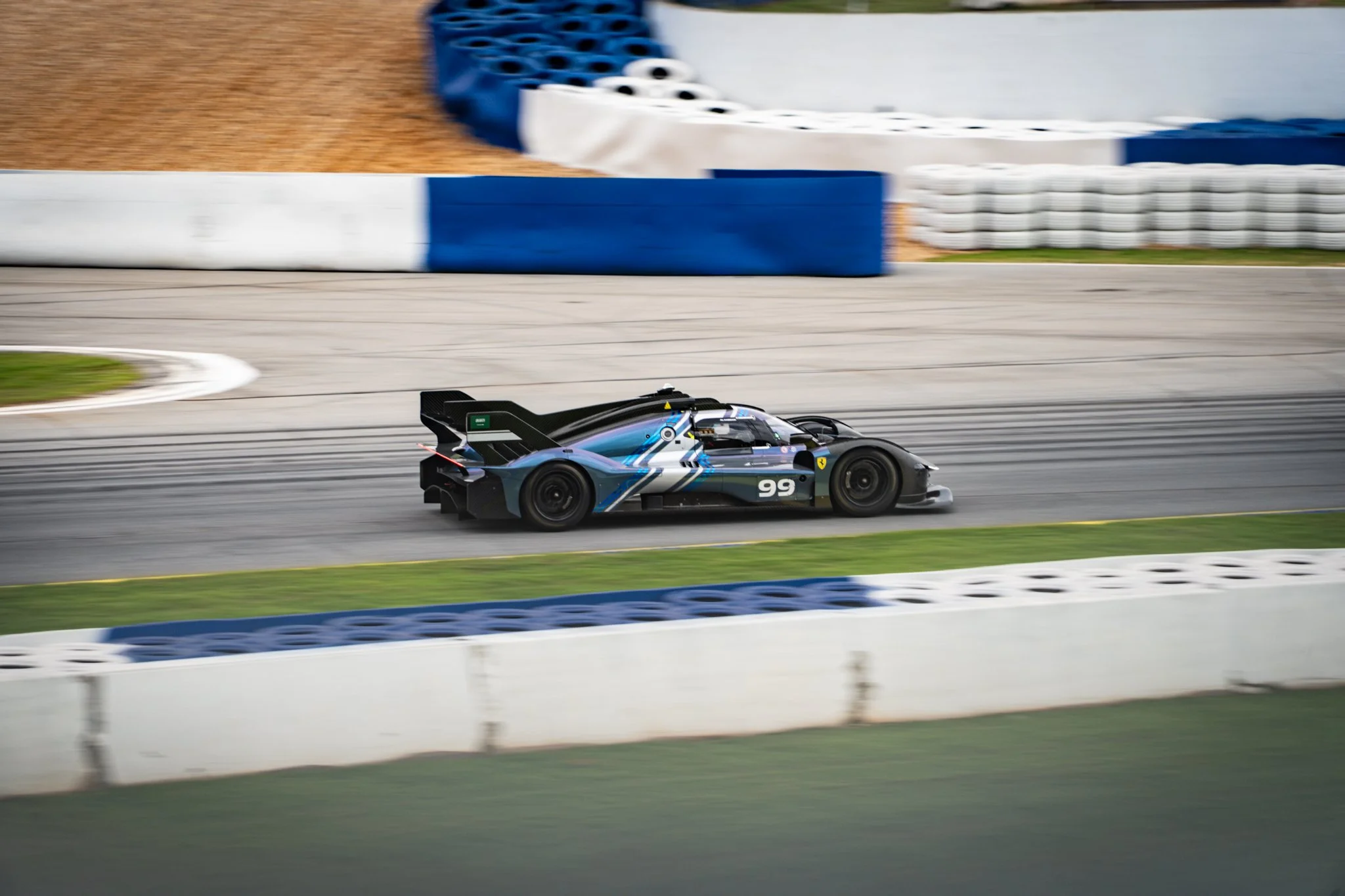 A race car on a race track, with a blue and white barrier and tire wall in the background.