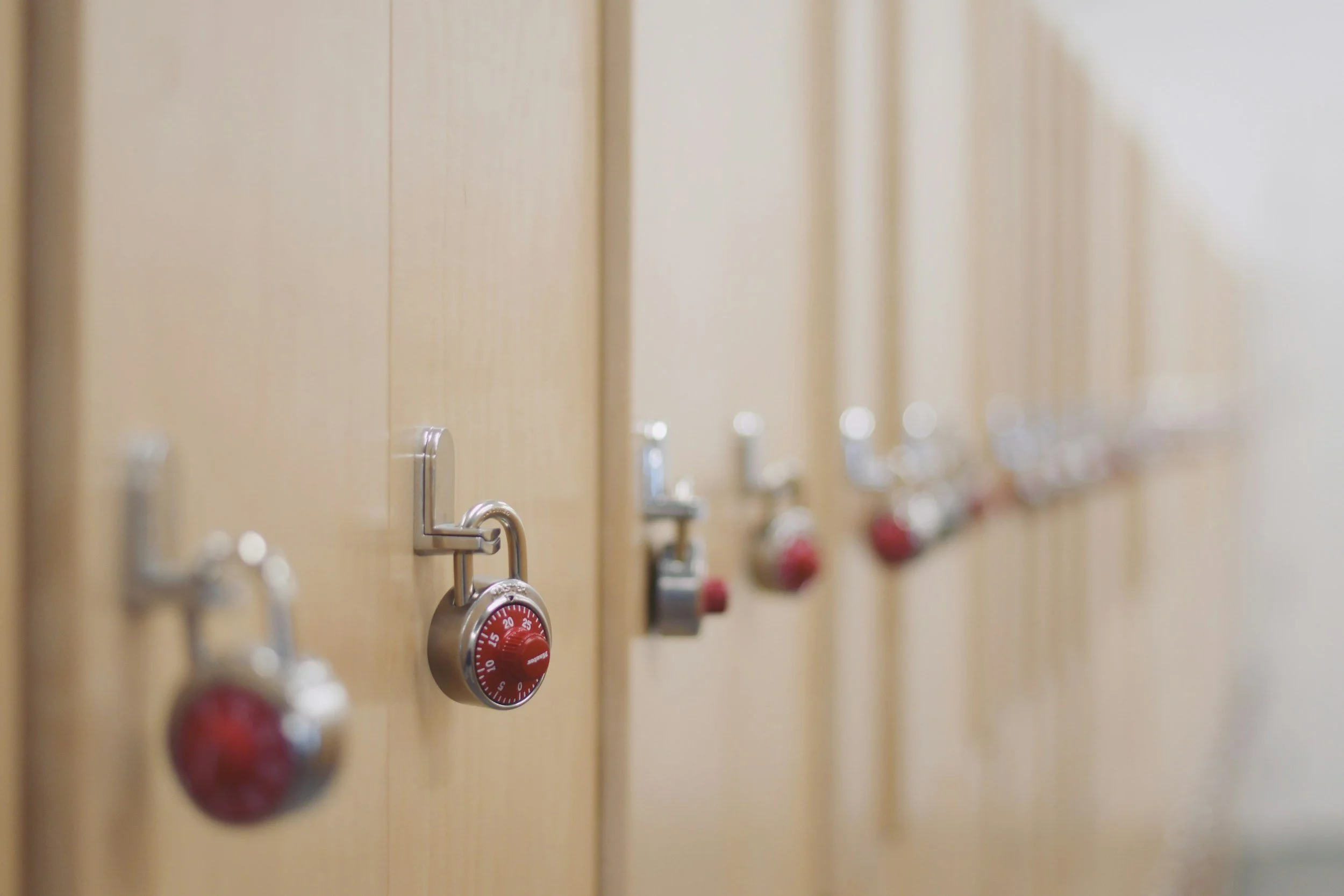 Close-up of beige lockers in a locker room with combination locks, some with red combination dials, and a few open doors.