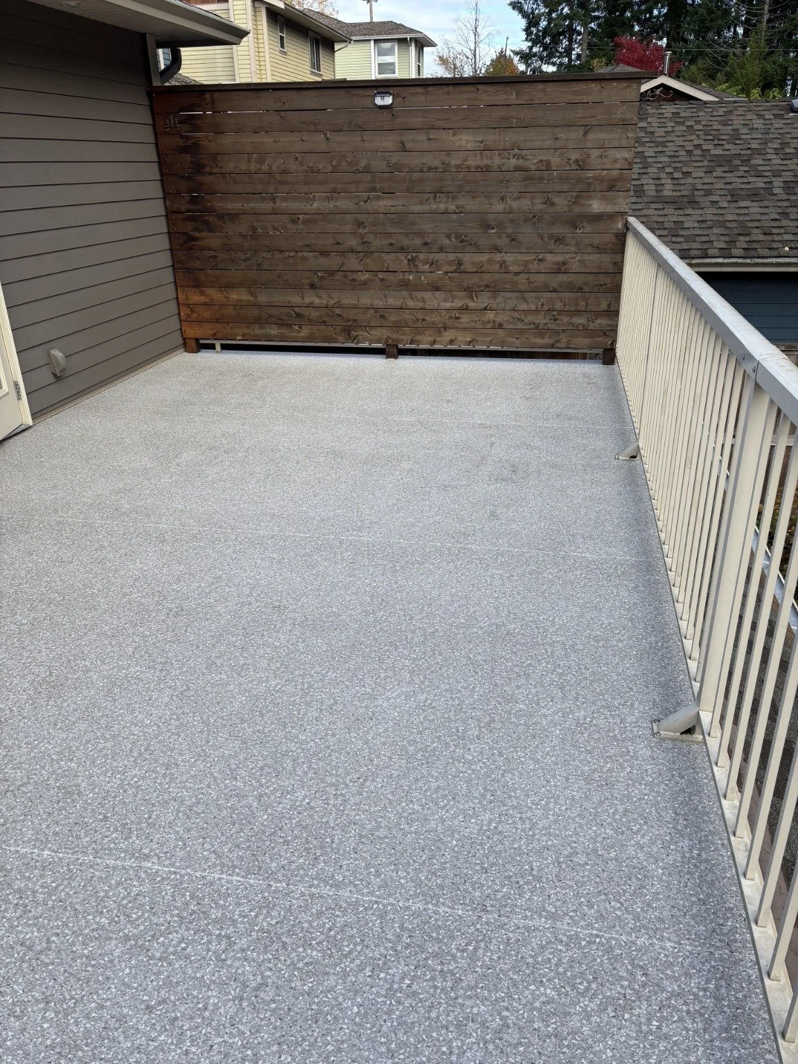 After: finished vinyl deck beside the house, with a wood privacy wall and metal railing.