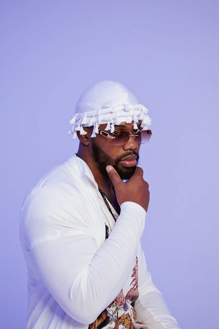 White outfit / purple background:
"Jacob Berry posing in an all-white streetwear look against a soft purple studio backdrop."