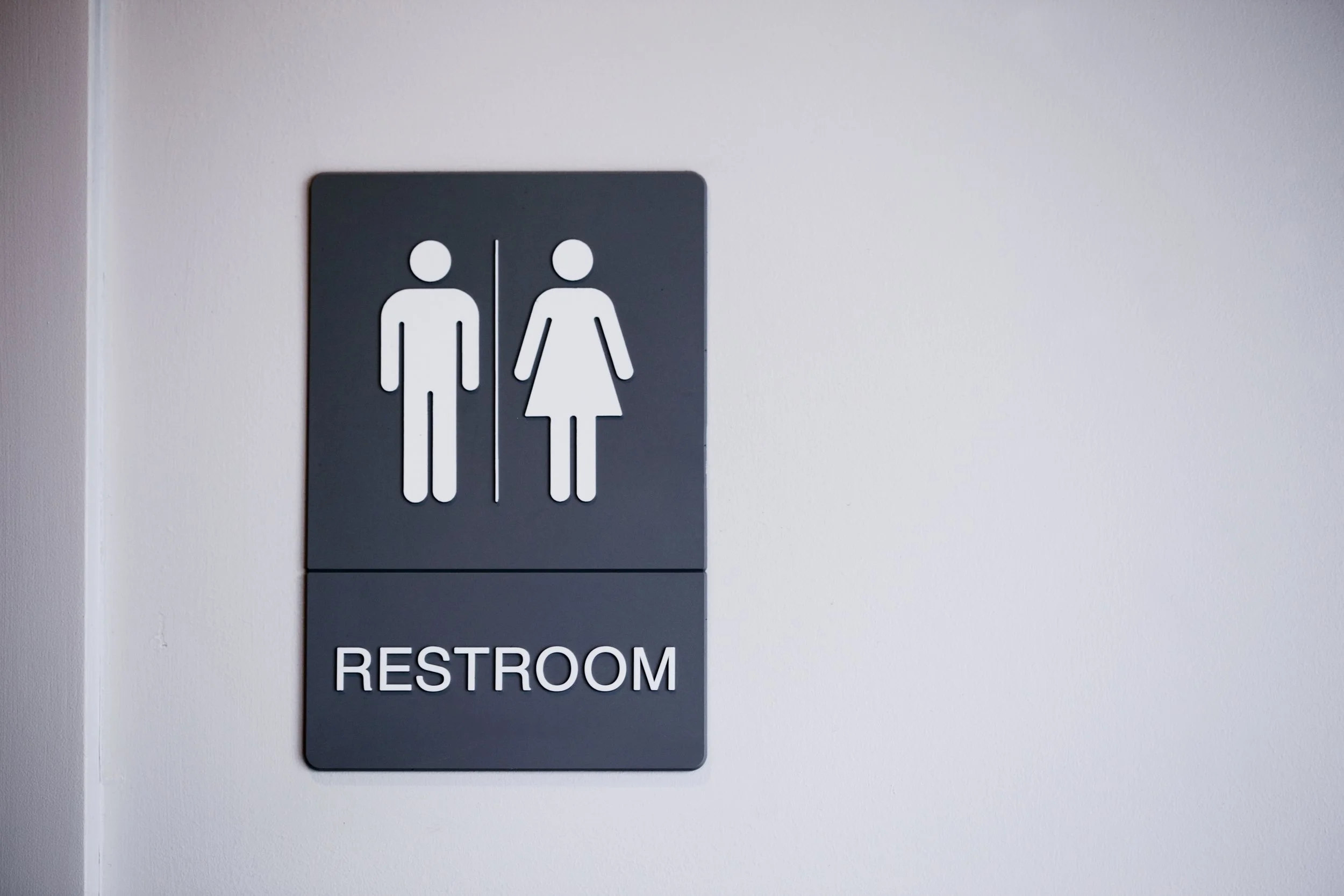 Sign indicating a restroom for men and women, mounted on a white wall.