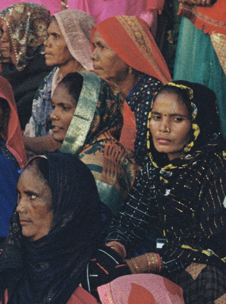Group of women dressed in traditional colorful clothing and headscarves, seated closely together in a social gathering. Taken by Olivia Ladesic in Delhi, India on 35mm film.