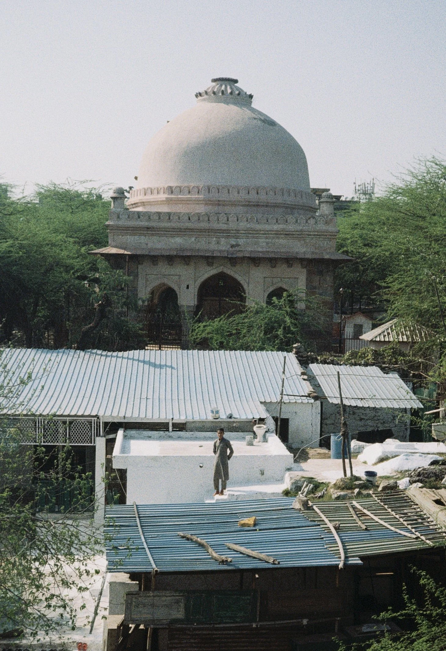 A mosque with a large white domed roof, intricate carvings, and a smaller dome on top, surrounded by green trees. Film shot by Olivia Ladesic.