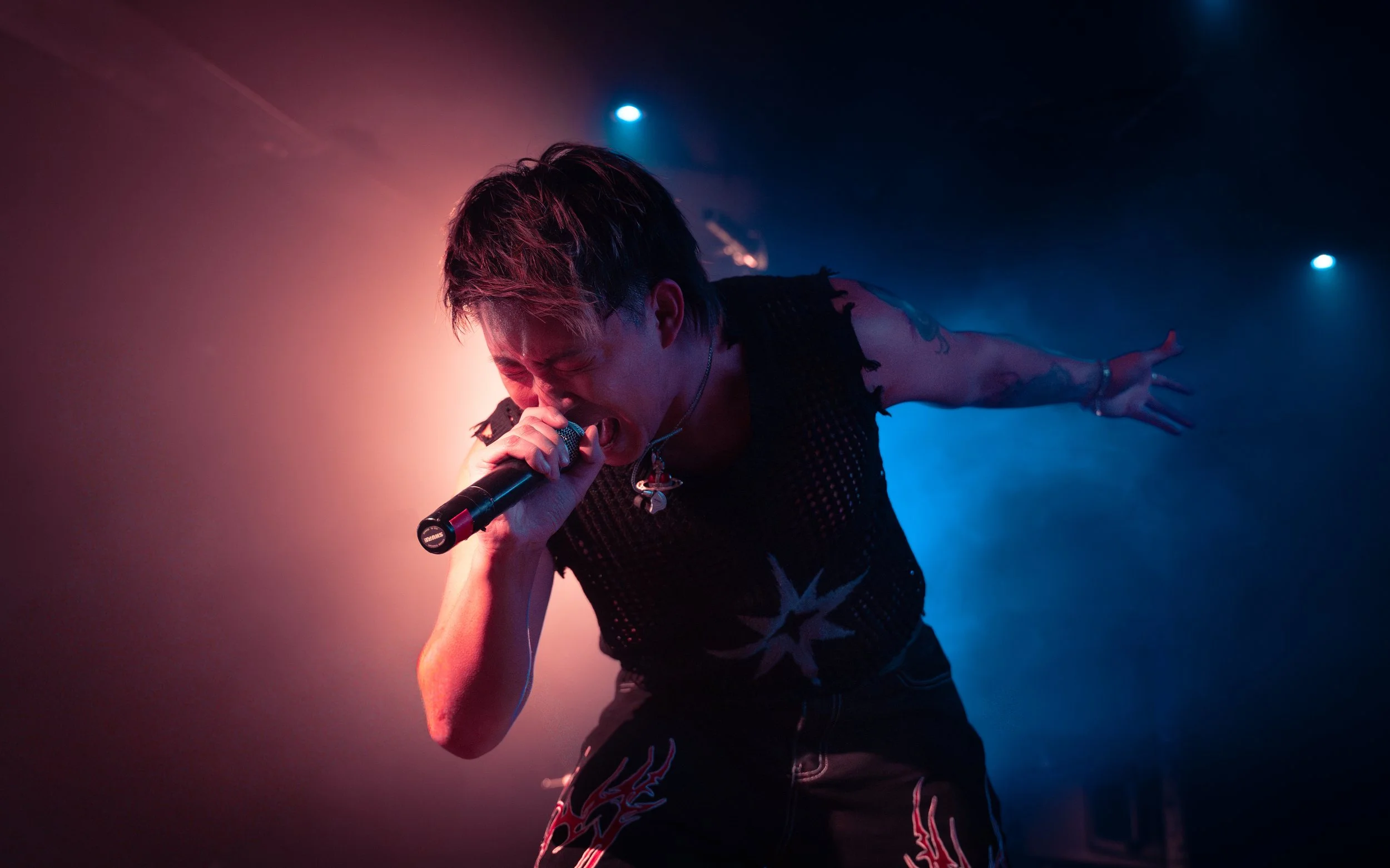 A male singer passionately performing on stage with colorful lighting, holding a microphone close to his mouth, and reaching out with his other arm.