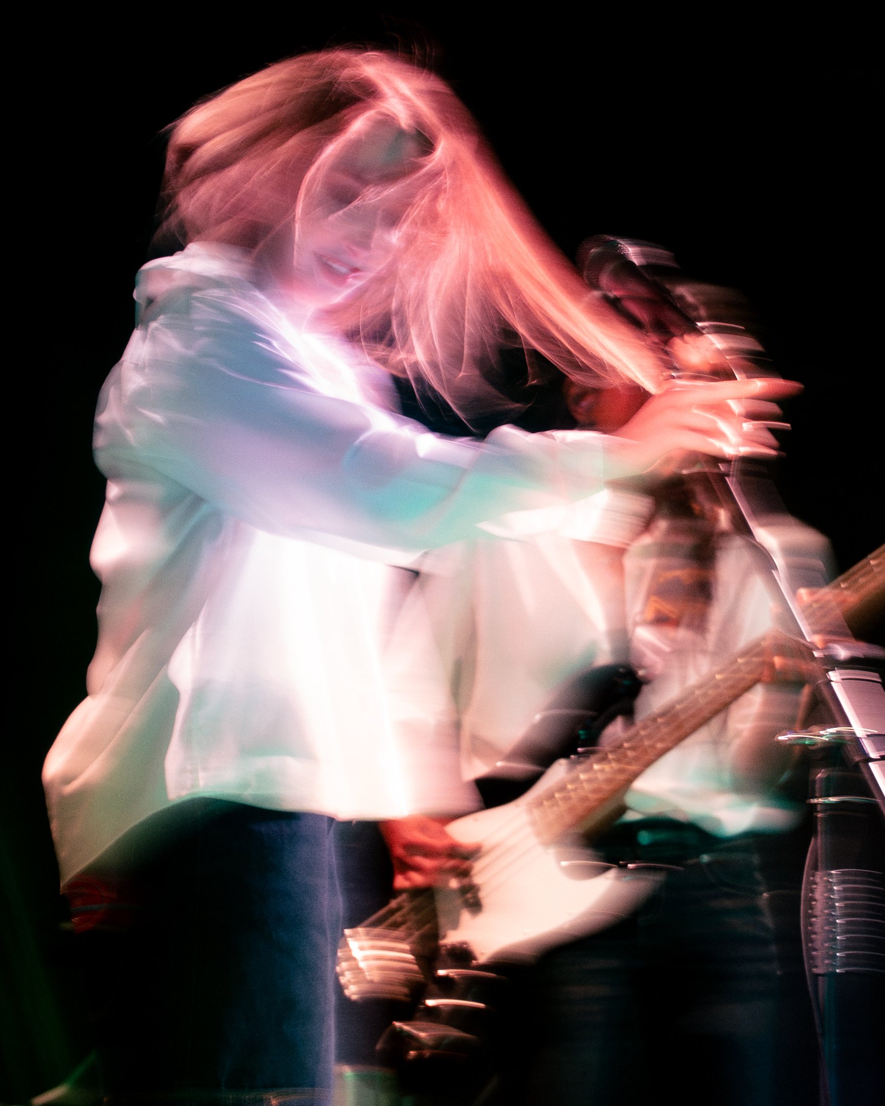 A person playing electric guitar on stage with pink and purple lighting, with motion blur making the scene appear dynamic and abstract.