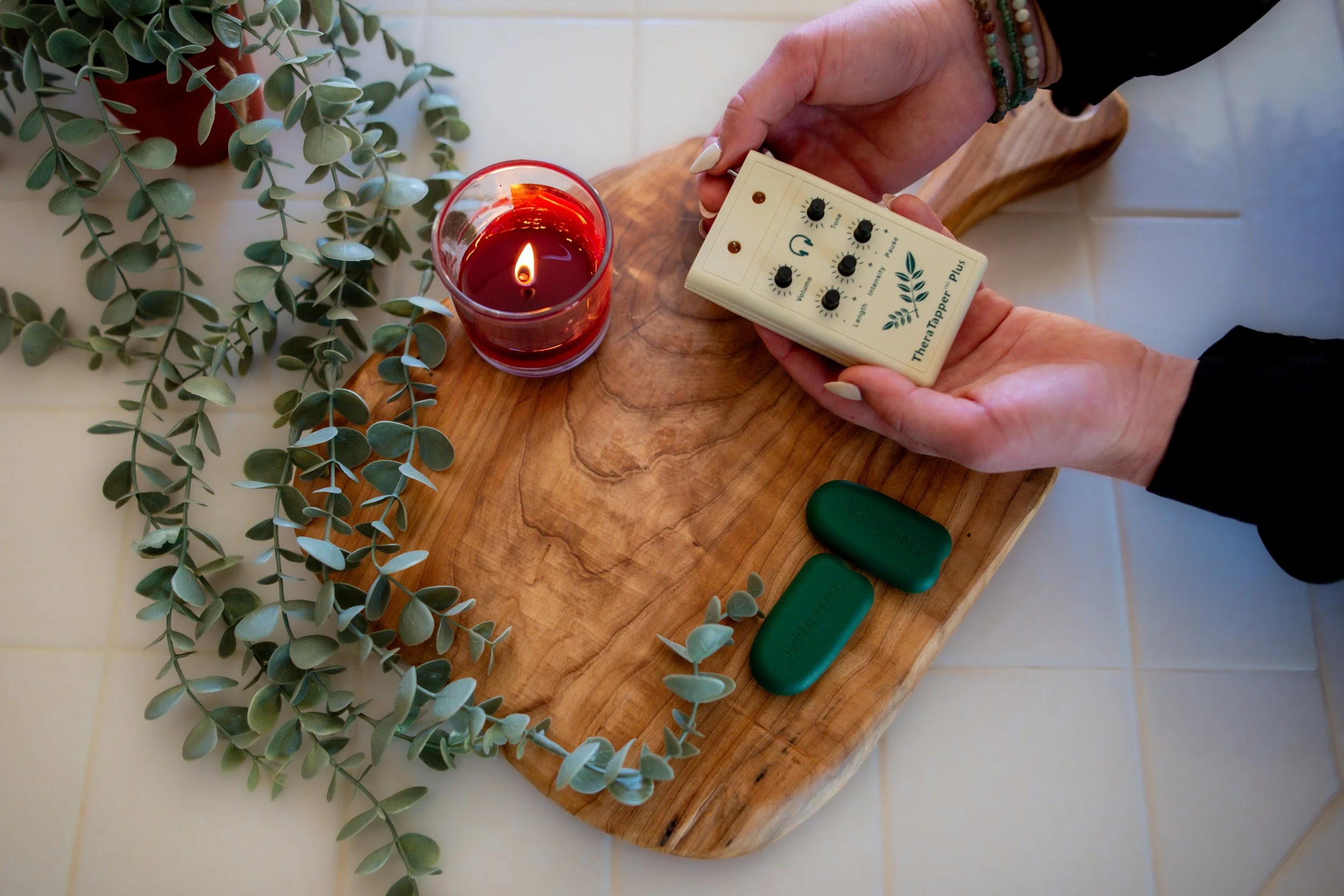 Person holding a white therapy tapper device with three control knobs and a connected green device with two prongs.