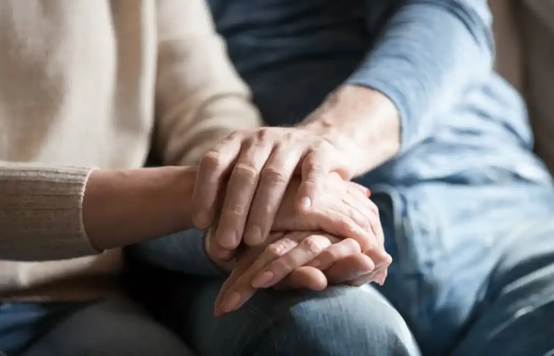 Two people holding hands, one person gently resting their hand on top of the other's hand.