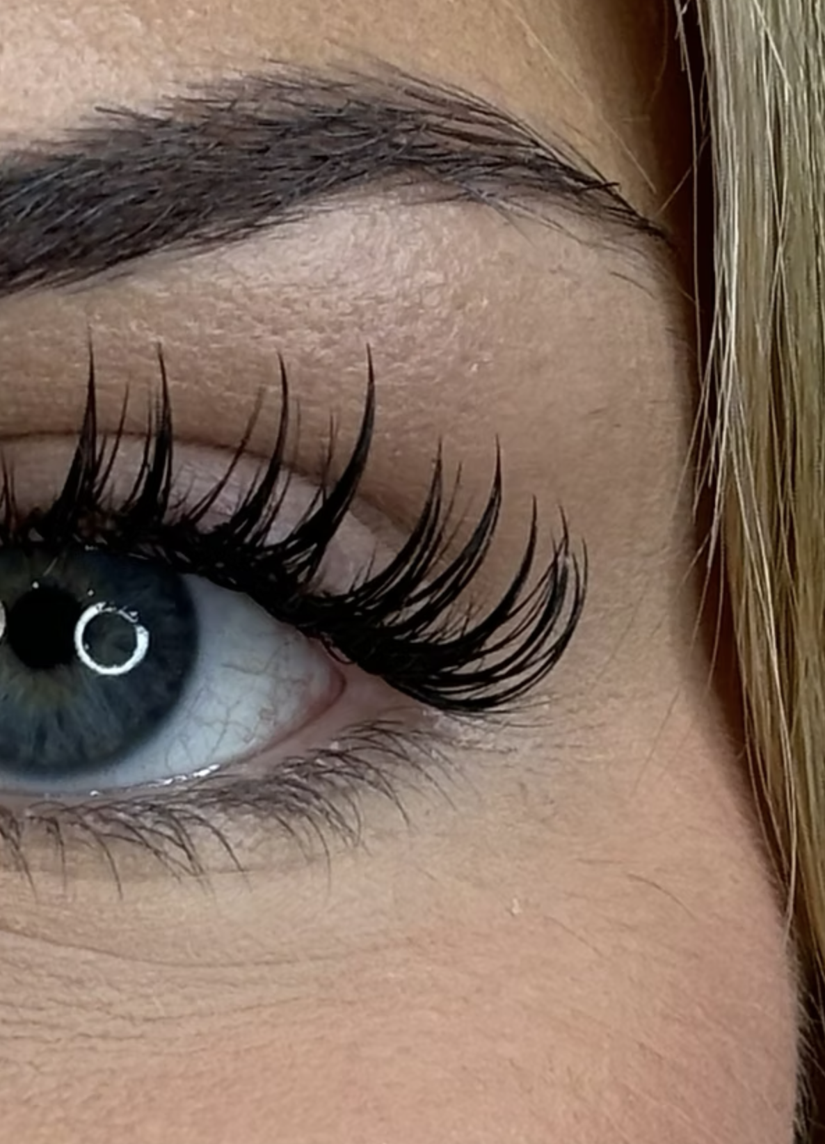 Close-up of a person's eye with long eyelashes, blue-green iris, and blonde hair.