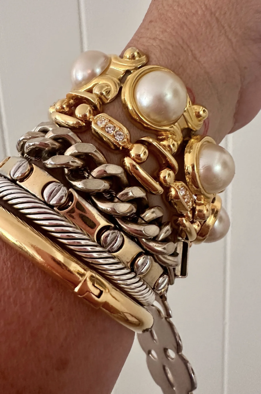 A person's wrist adorned with multiple gold and silver bracelets, including pearl and diamond accents.