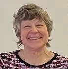 A smiling woman with short, wavy gray hair wearing a patterned blouse.