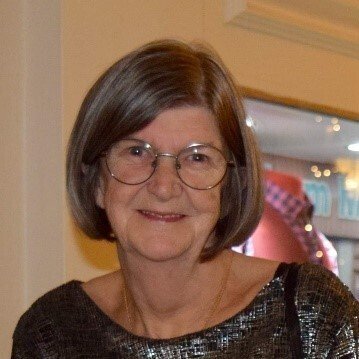 A woman with short brown hair, wearing glasses and a black sequin top, smiling indoors.