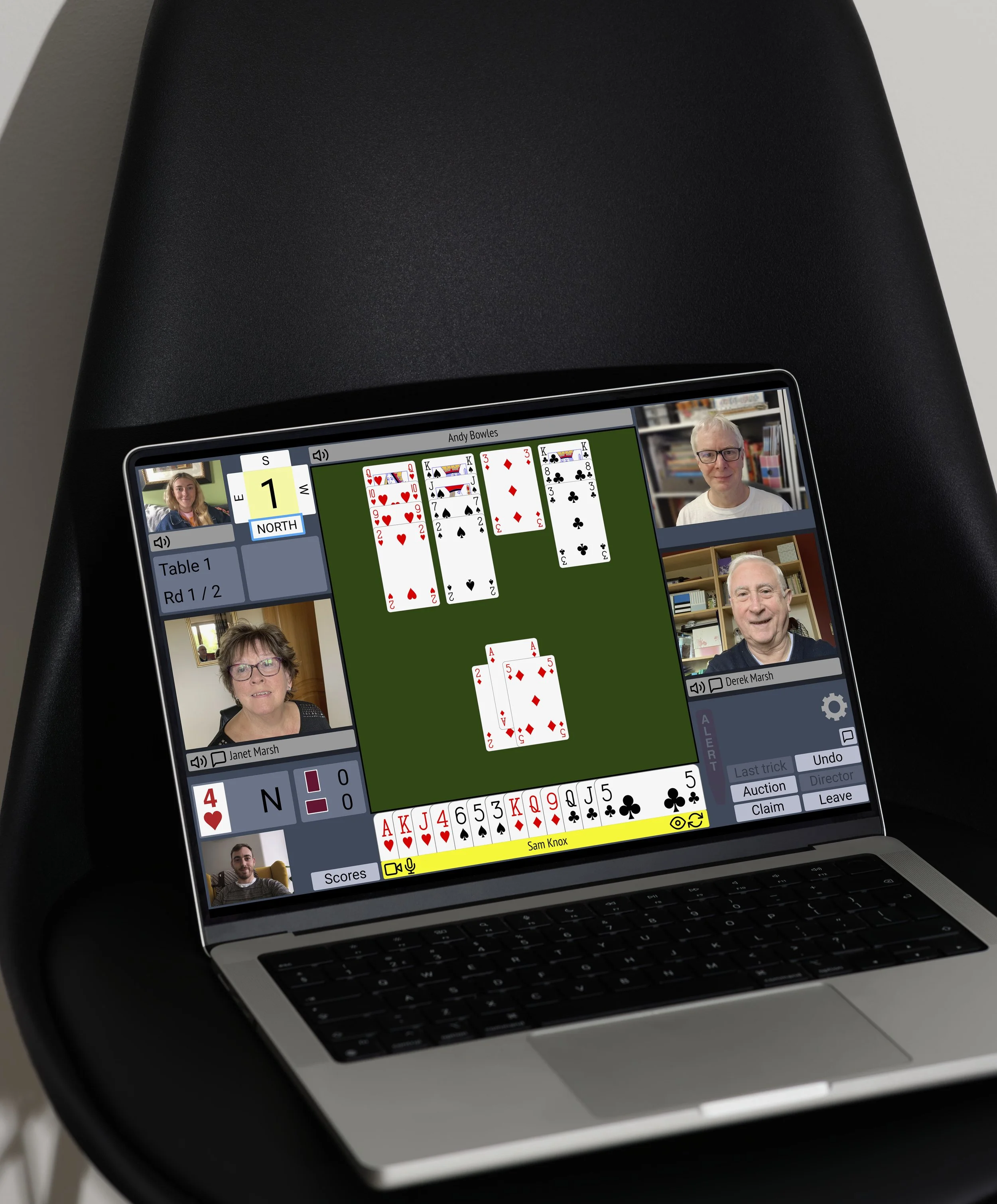 A laptop displaying an online card game with multiple players and a central tableau of played cards, in a virtual meeting setting.