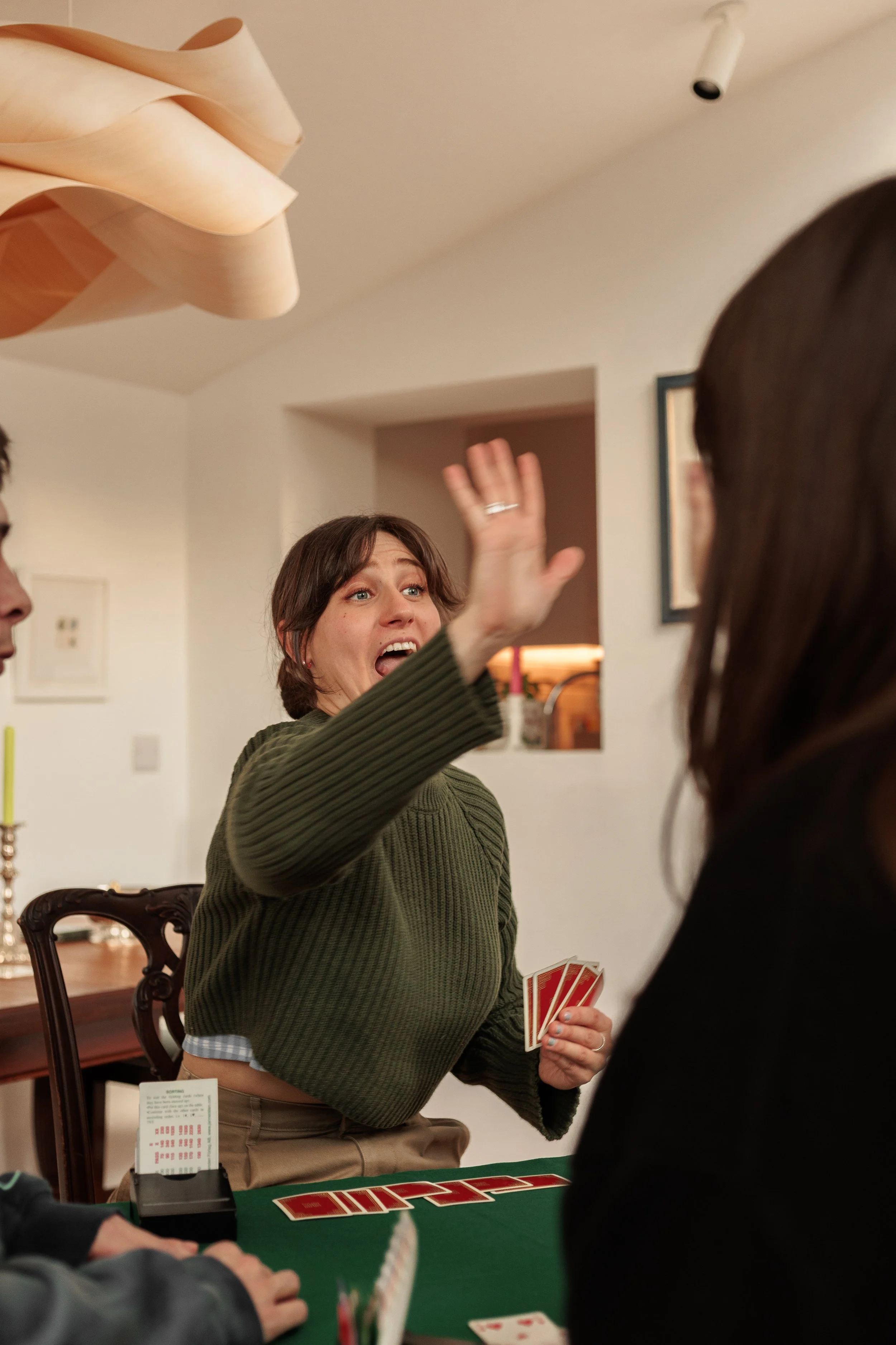 People playing a game of Uno at a dining table in a home, with one woman enthusiastically throwing her hand in the air.