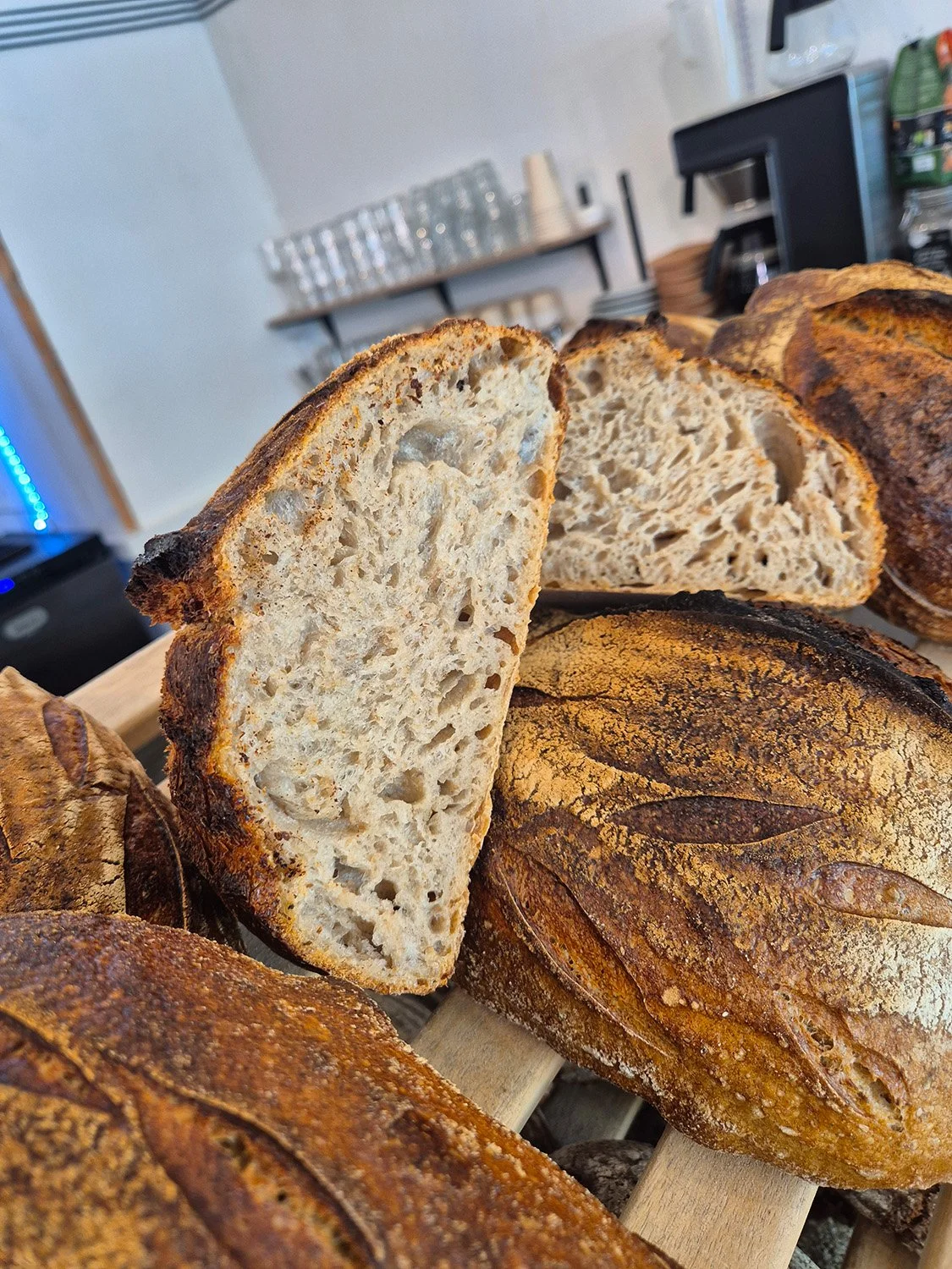 Verschiedene Brote auf einem Holzbrett, darunter ein aufgeschnittenes rustikales Sauerteigbrot mit luftiger Krume.