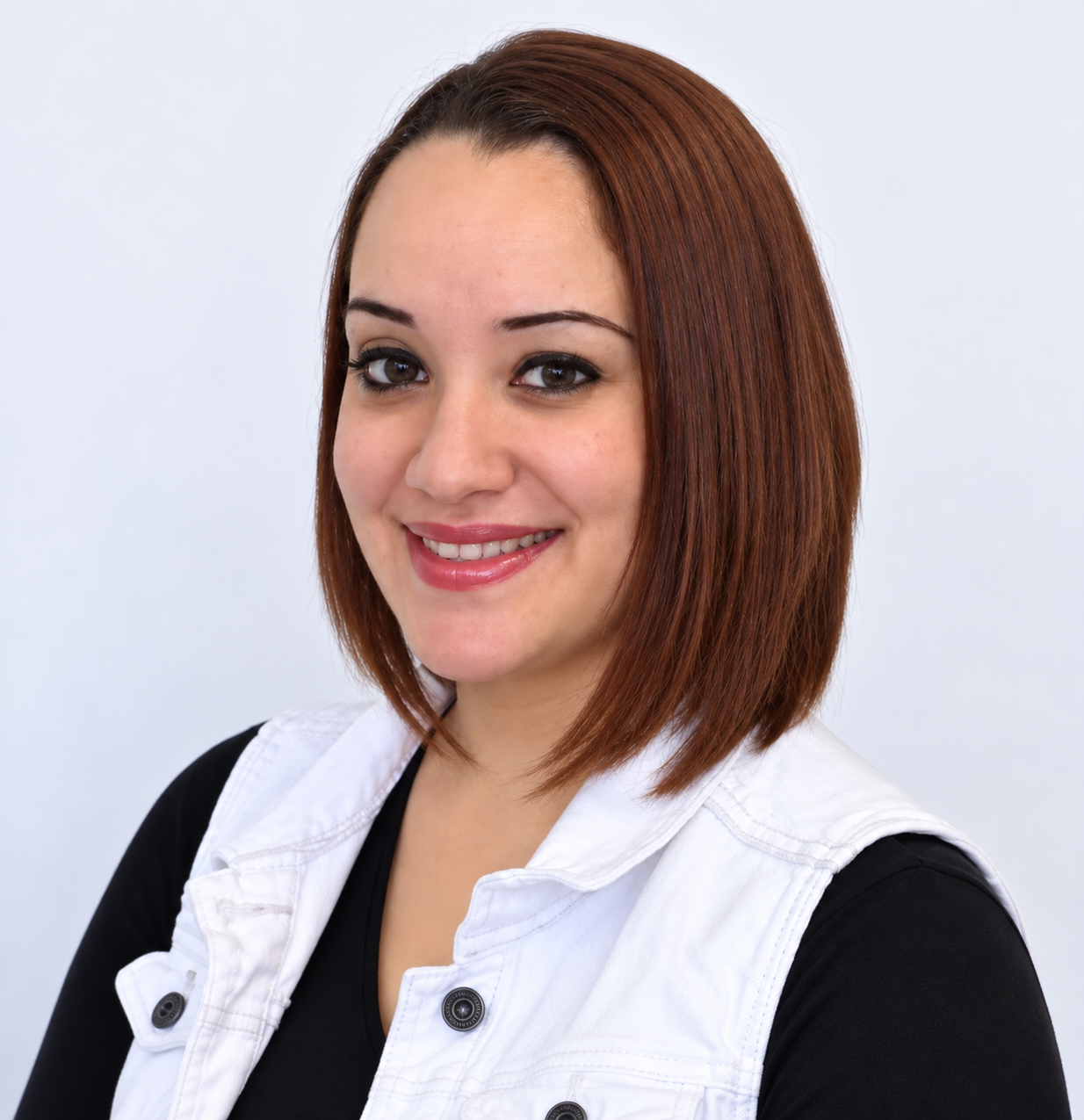 Portrait of a young woman with straight, shoulder-length reddish-brown hair, smiling, wearing a black top and a white sleeveless vest, against a plain white background.