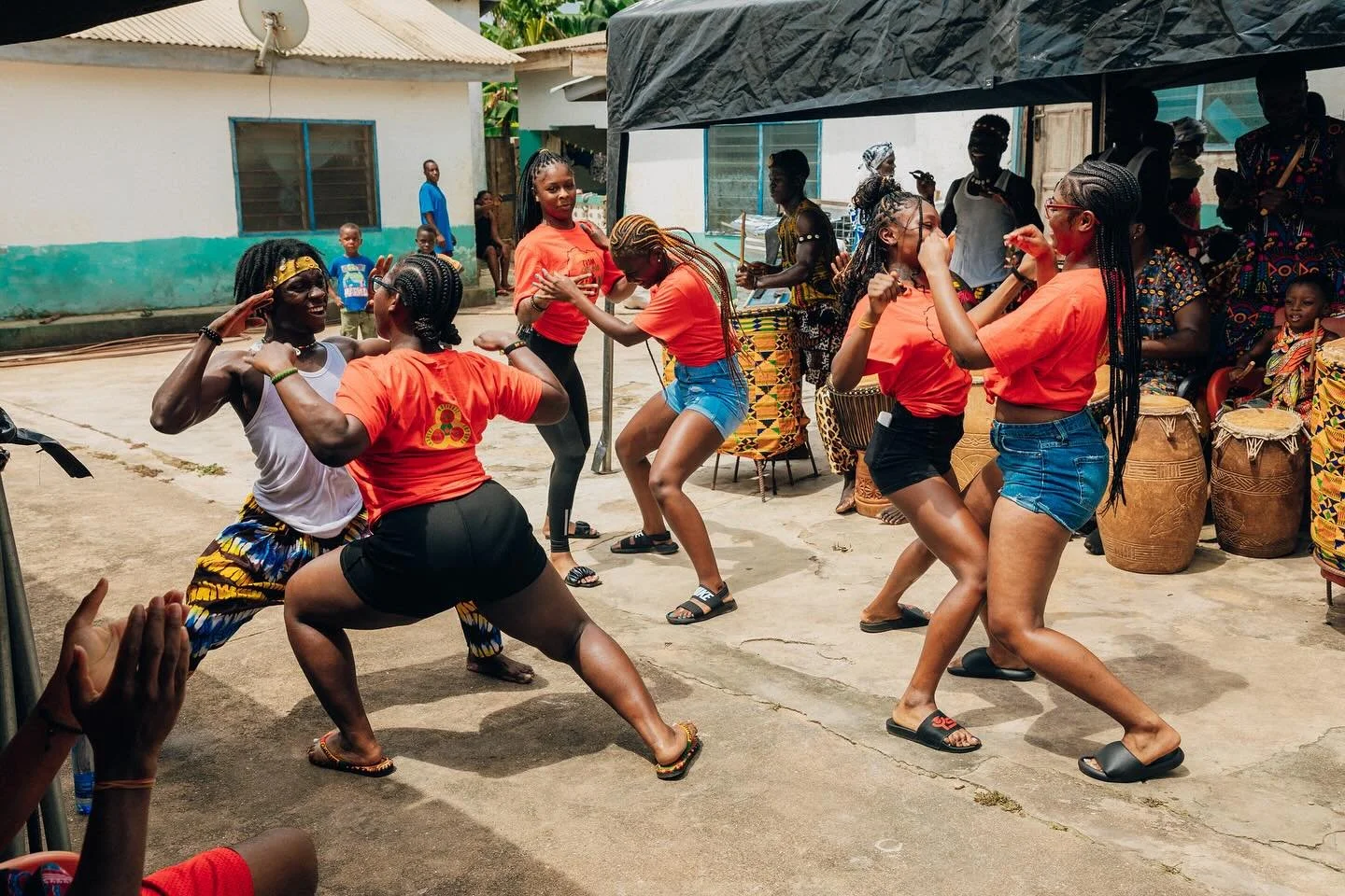Group of women dancing and enjoying themselves outdoors during a cultural celebration, with musicians playing traditional drums in the background.