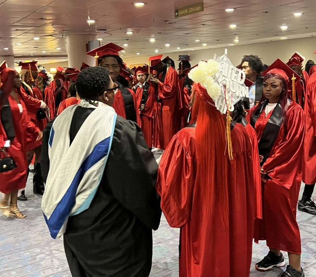 Graduates in red caps and gowns at a graduation ceremony, conversing in a large indoor space.