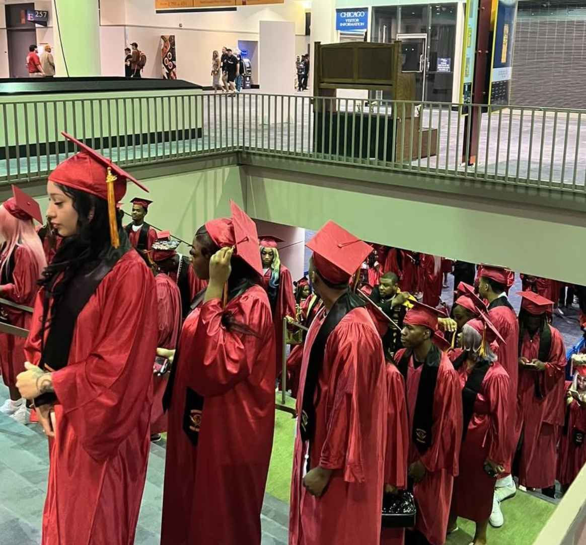 Group of graduates dressed in red caps and gowns standing in line inside building.