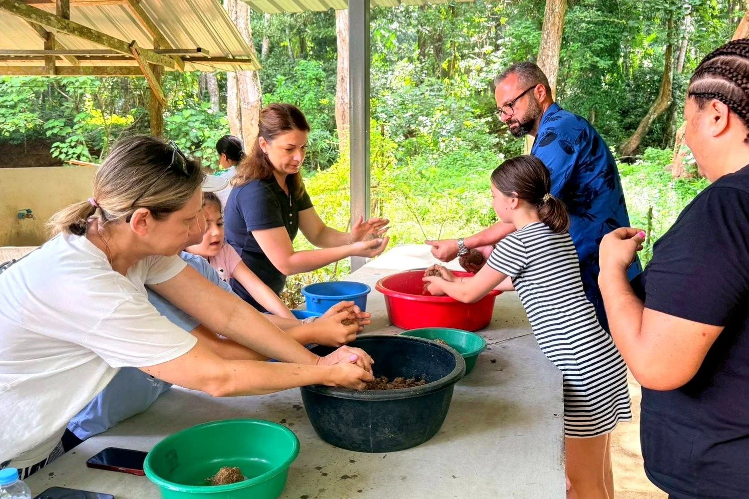 Guests and children preparing food for the elephants together at a covered table in the Krabi jungle