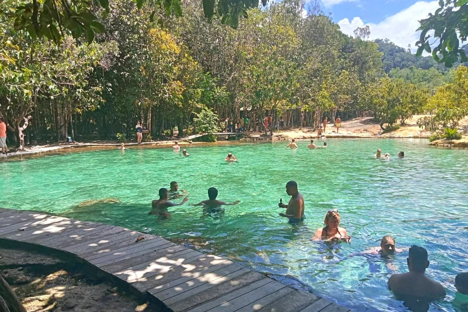 Tourists swimming in the clear green water of Emerald Pool in Krabi
