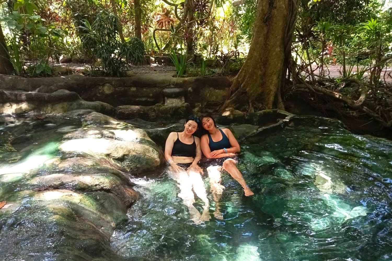 Two women relaxing in a natural hot spring pool surrounded by jungle in Krabi