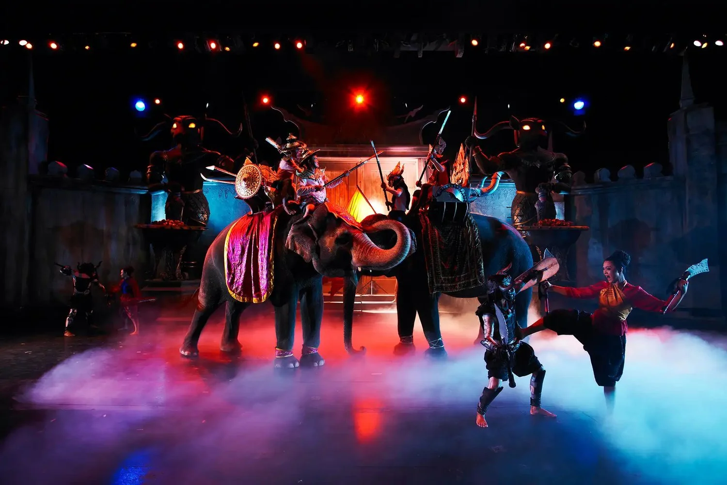 Two elephants with riders and performers on stage at the Phuket FantaSea show
