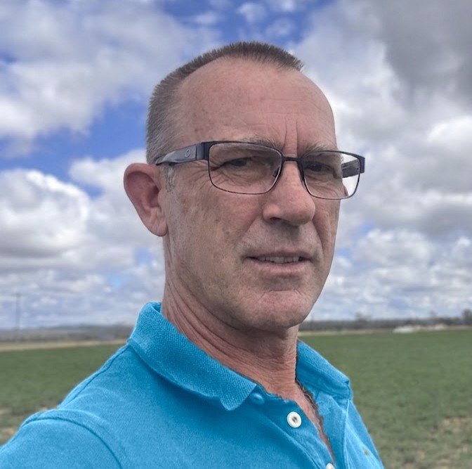 Outdoor portrait of Andrew, Practice Manager and Work Pathways Coach, wearing glasses and a blue shirt against an open landscape, representing practical, approachable support for employment pathways and workplace participation.