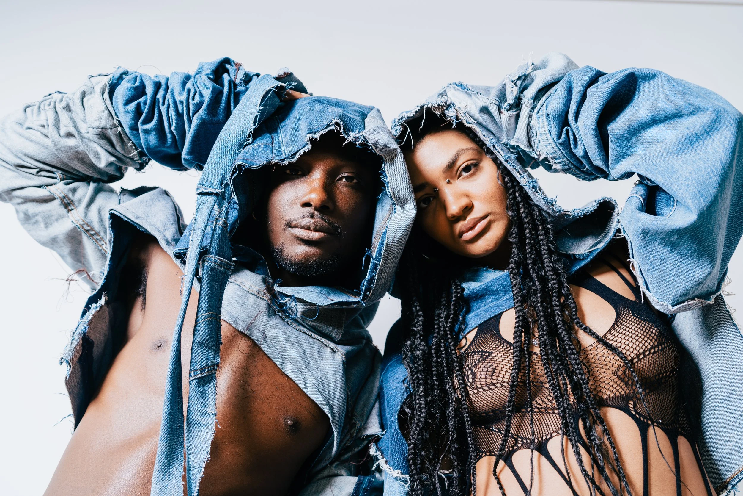 Two models wearing distressed denim jackets and clothing, posed closely together against a plain background.