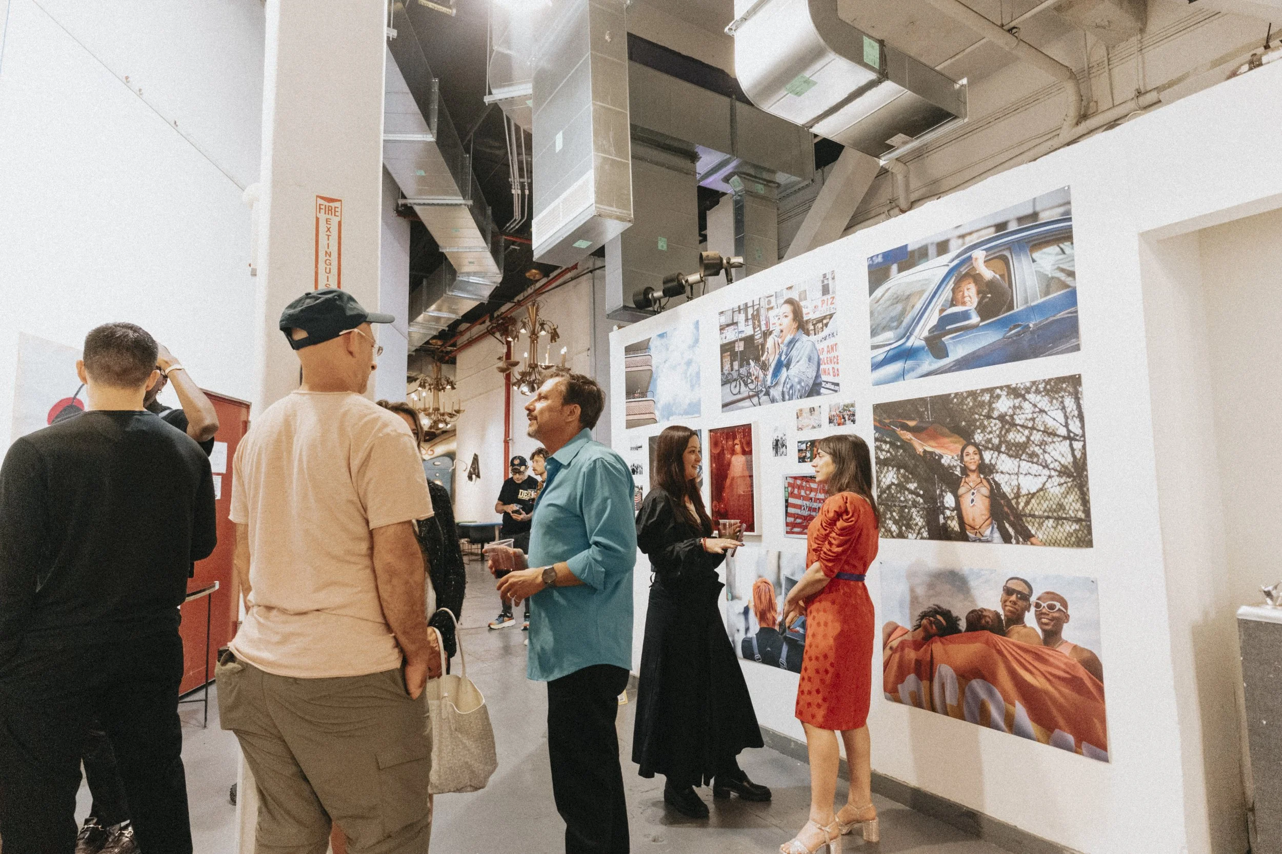 People attending an art gallery exhibit, viewing and discussing photographs displayed on a white wall.