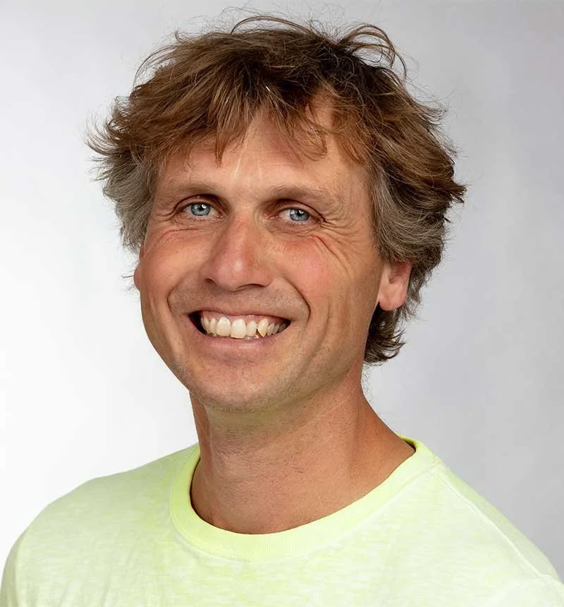 Portret van een lachende man met lichtbruin haar en blauwe ogen, droeg een lichte groene shirt, witte achtergrond.