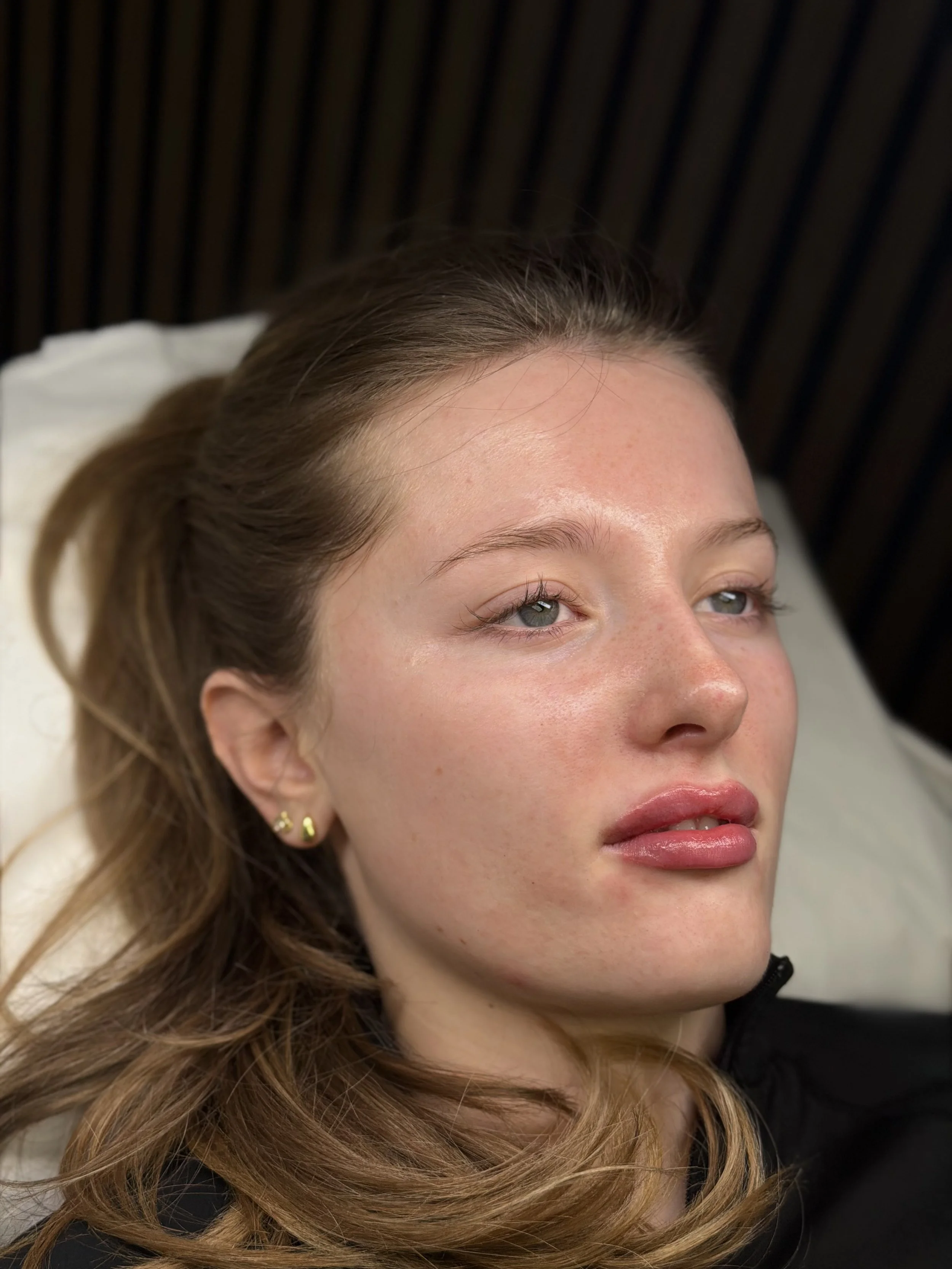 Close-up of a woman with light skin, blue eyes, and long wavy brown hair lying down with her eyes open.