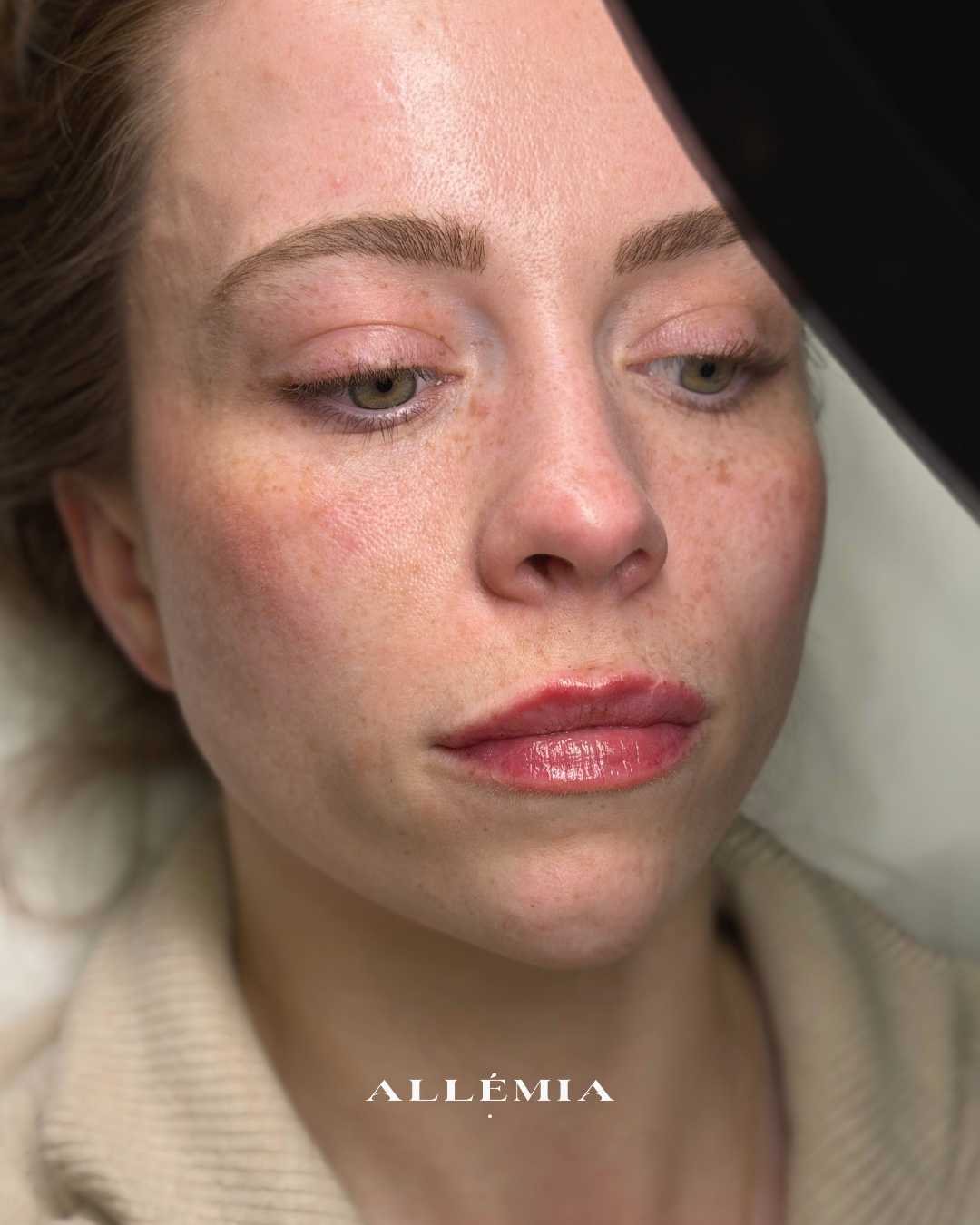 Close-up of a woman with natural makeup and freckles, lying down with her eyes slightly open.