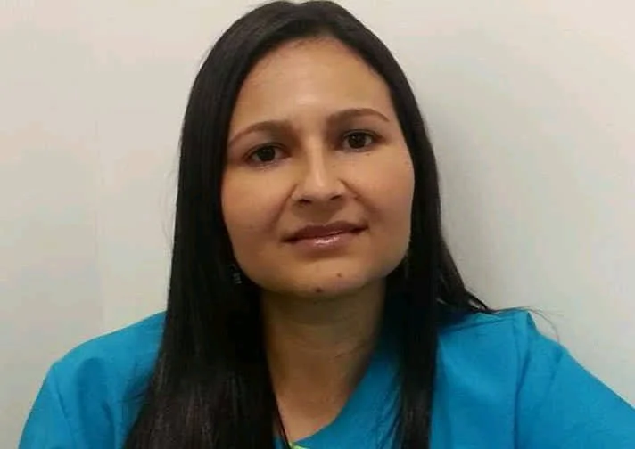 Retrato de una mujer con cabello largo y oscuro, usando una camisa azul, frente a fondo blanco.