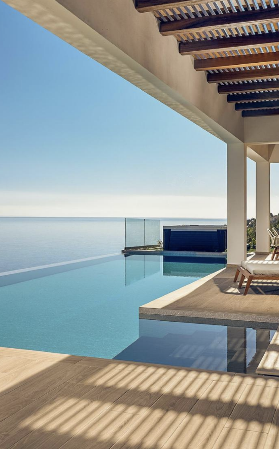 Luxury infinity pool overlooking the ocean with lounge chairs and modern architecture under a wooden pergola