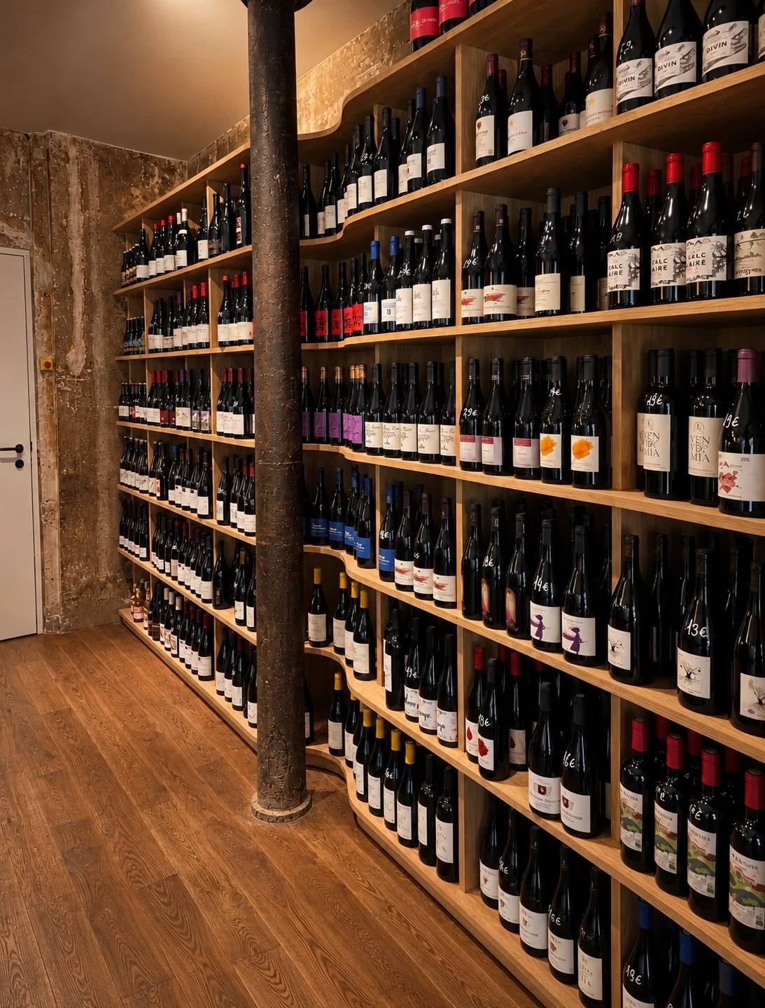 Rayonnage en menuiserie sur mesure avec forme vague et ondulé rempli de bouteilles de vin dans une cave à vins, fondation paris 11eme , avec un poteau en métal au centre.