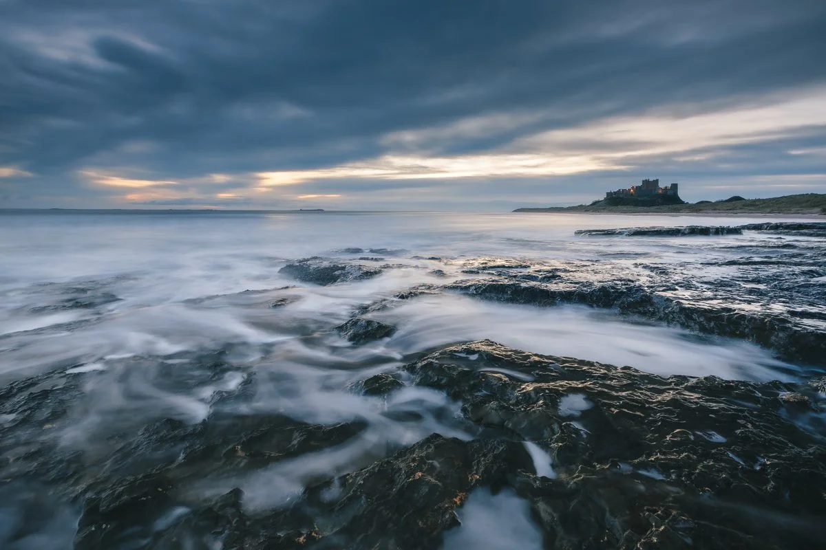 Bamburgh Castle on a moody morning, a steady flow of water over the rocks to enhance the scene.