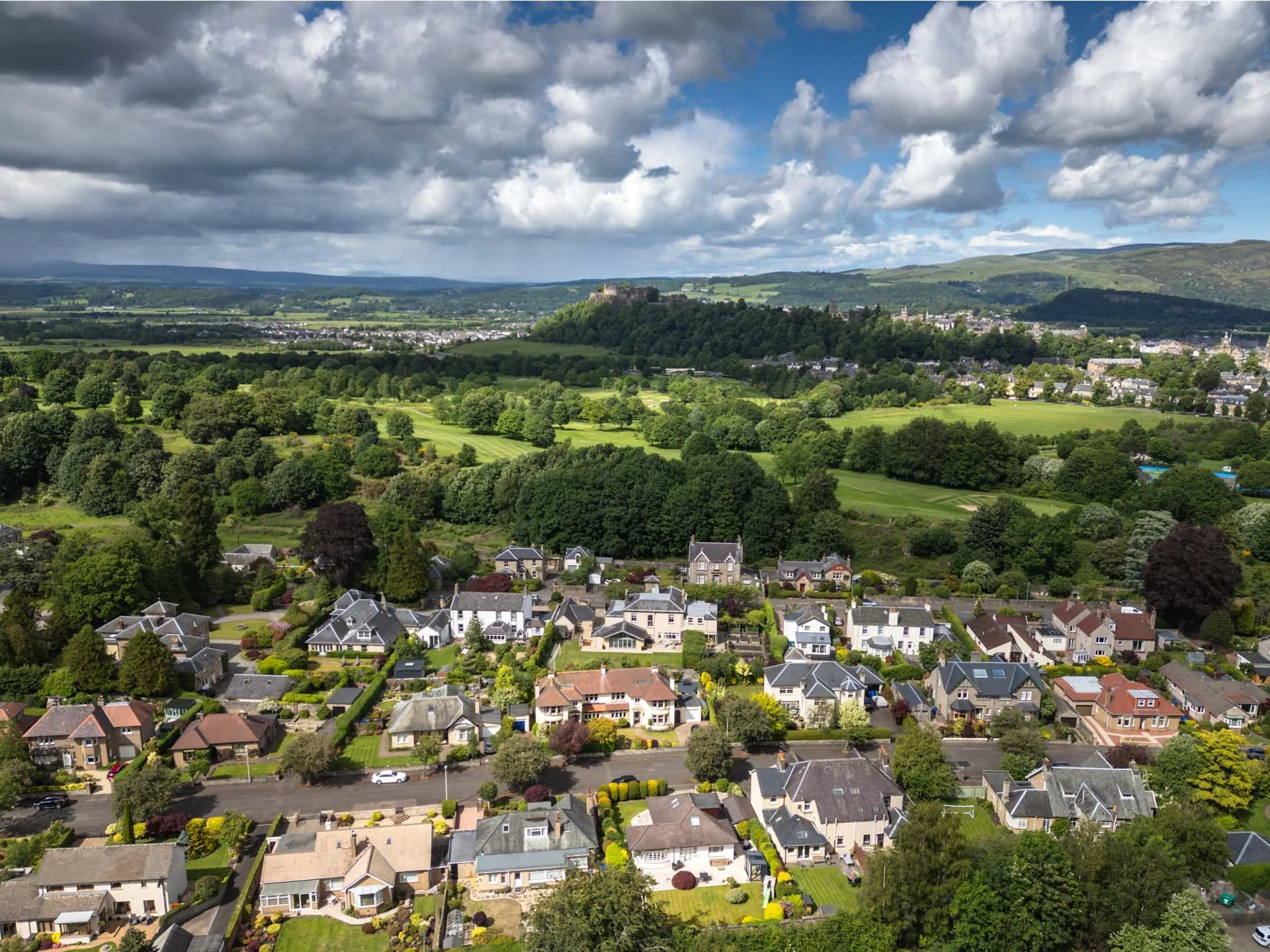 A scenic view of a town surrounded by lush green trees and rolling hills under a partly cloudy sky.
