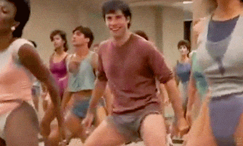 A group of people dance together in a room, smiling and enjoying themselves.