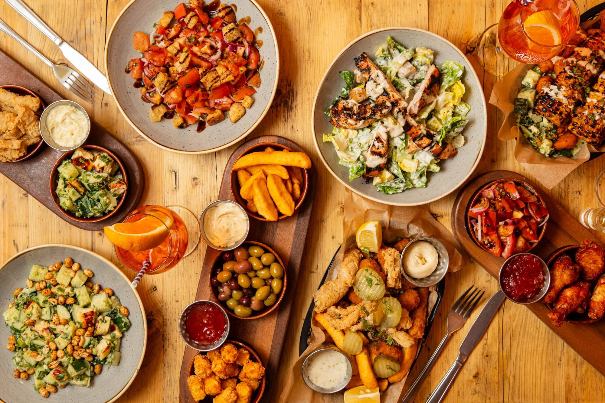 Various dishes of salad, fried foods, olives, and drinks on a wooden table.