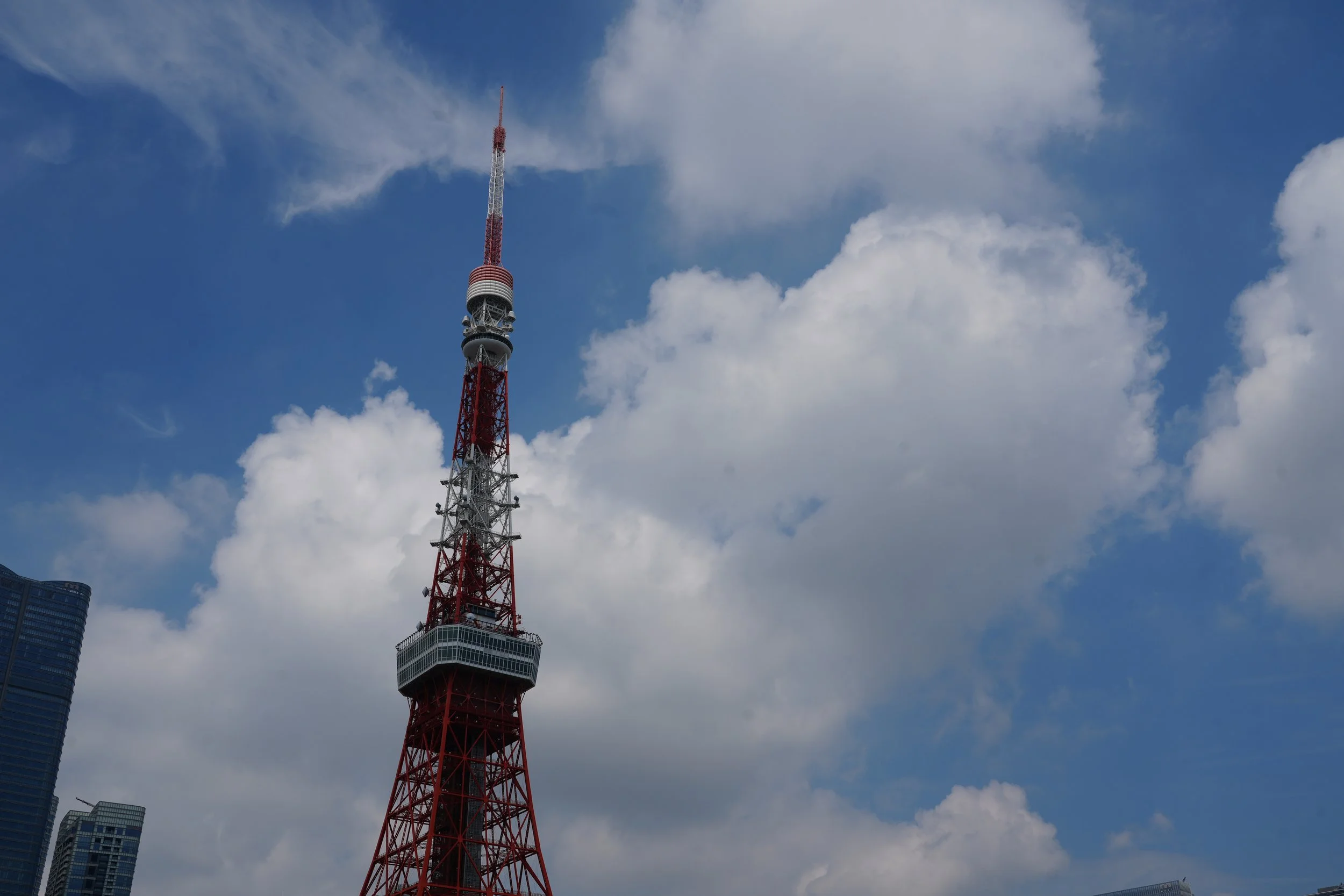 A tall red and white communication tower with multiple antennas and observation decks, set against a blue sky with scattered clouds.