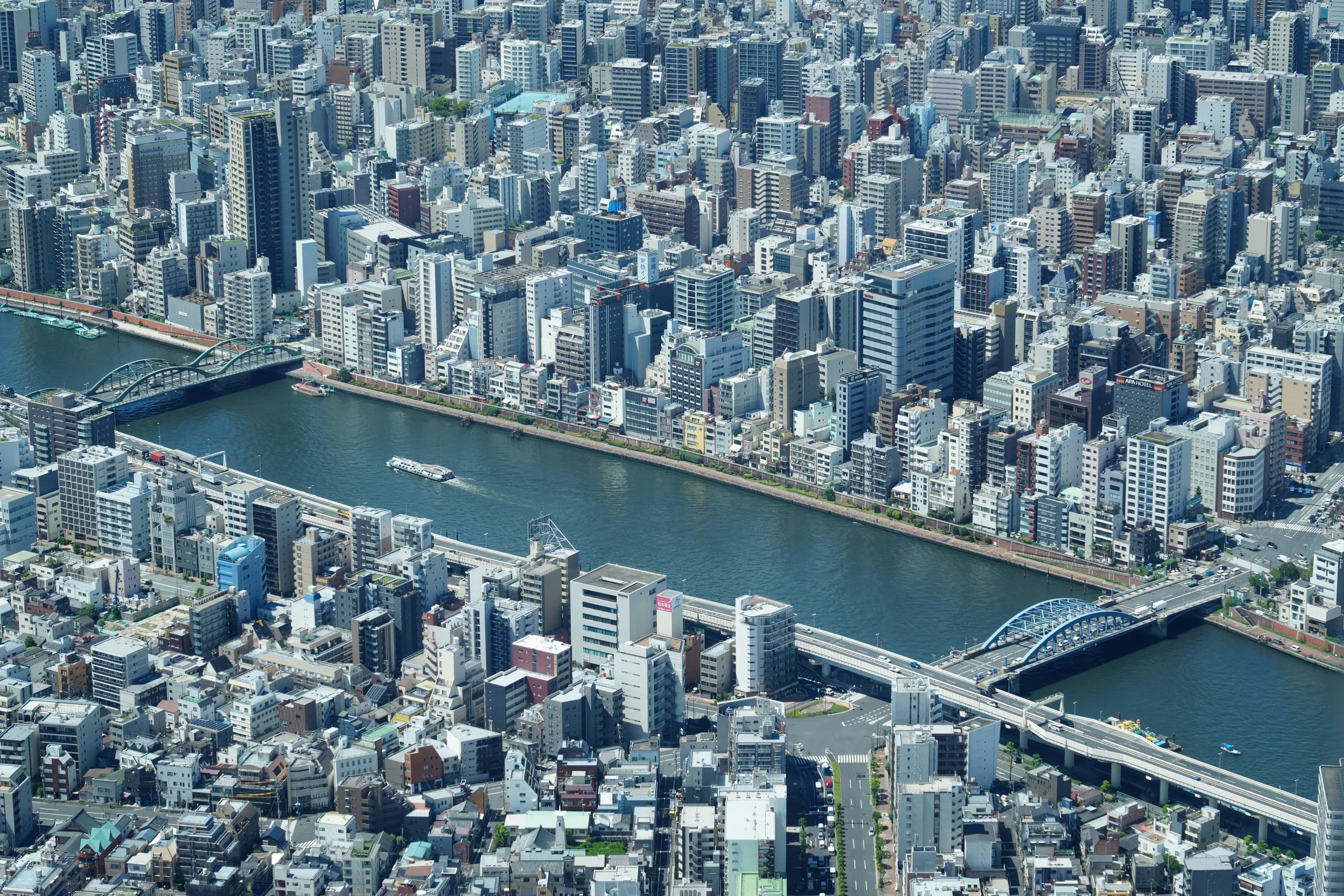 Aerial view of a dense urban area with numerous high-rise buildings along a river with bridges and boats, showcasing a cityscape.