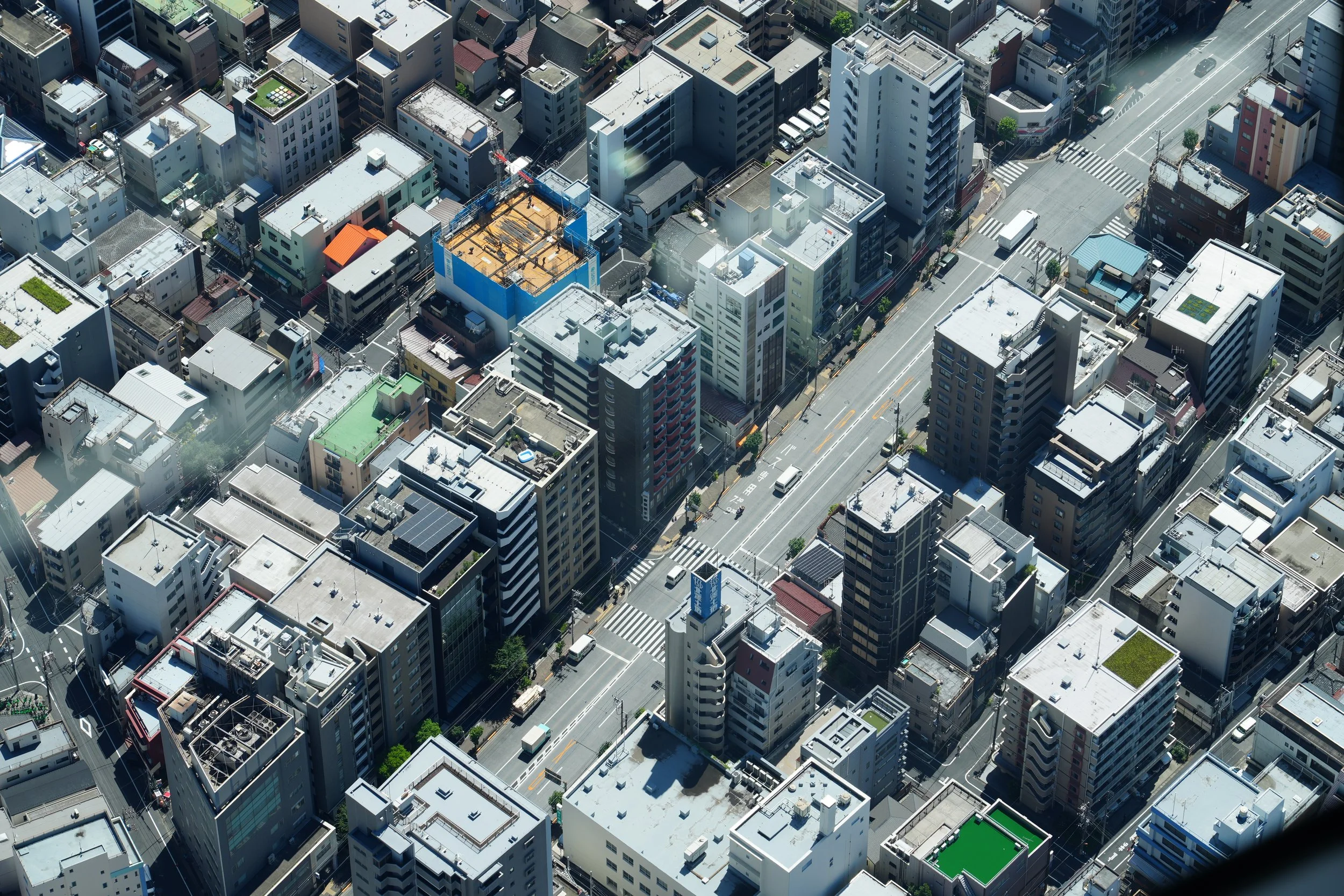 Aerial view of a densely packed city with numerous high-rise buildings, roads, and some green rooftop spaces.