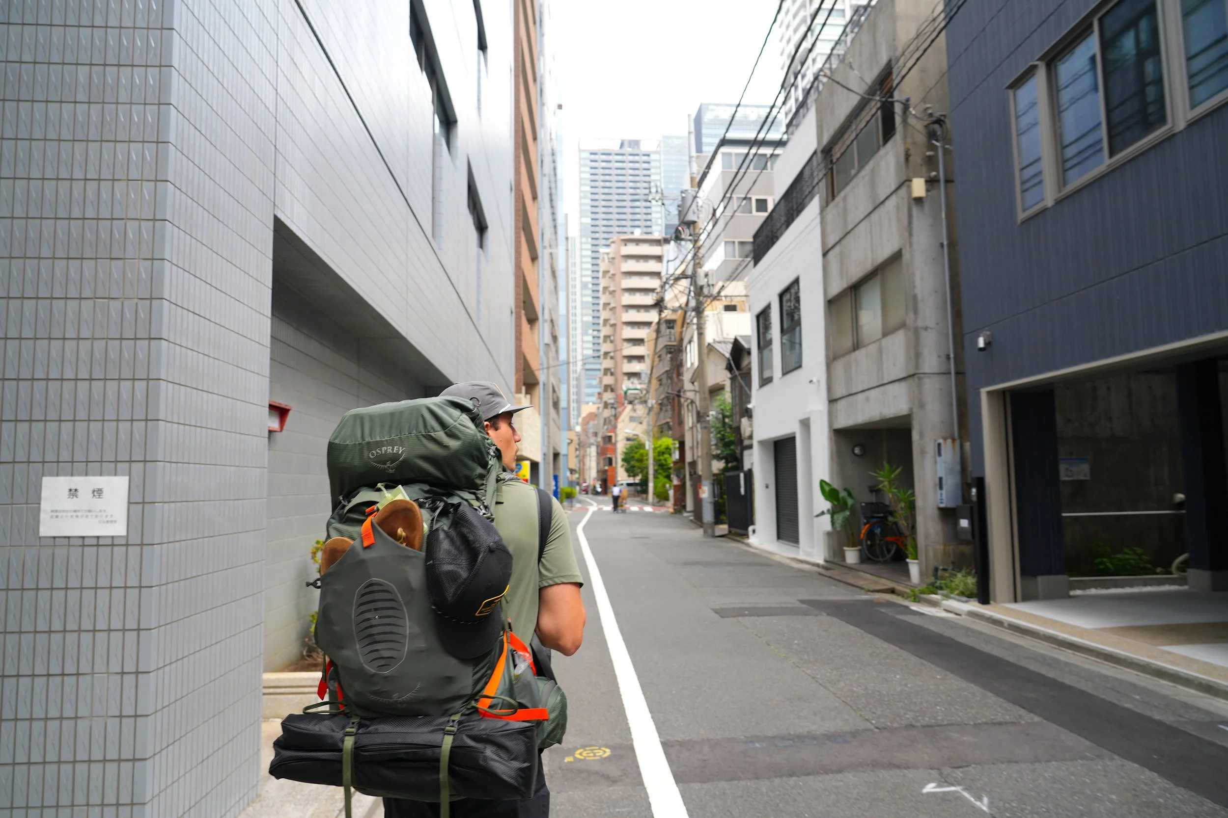 A person with a backpack walking down a narrow city street lined with tall buildings.