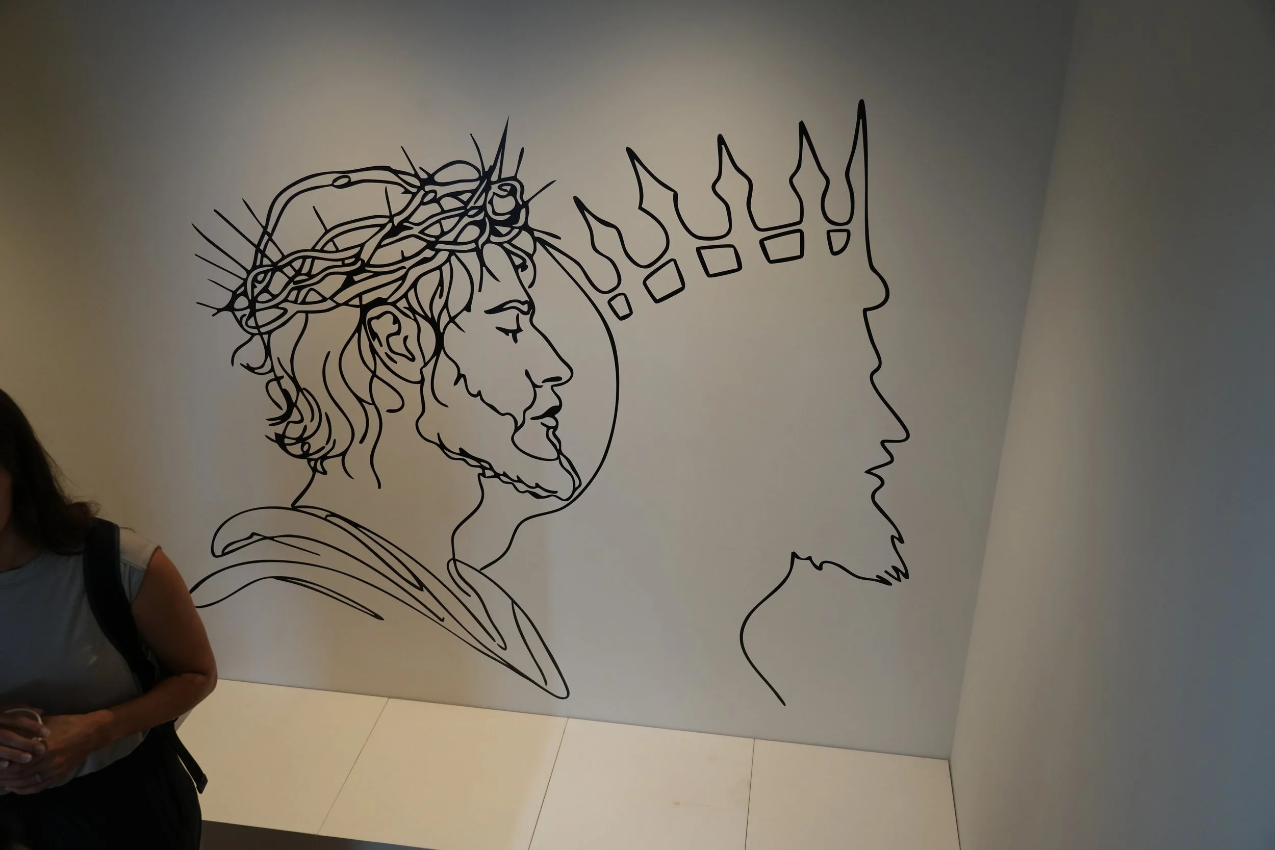 Wall art featuring a black line drawing of a profile of a man with a beard and crown of thorns, facing another profile outline of a face.