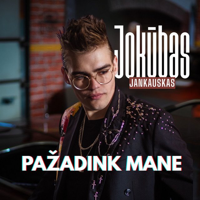 A young man with styled brown hair and glasses, wearing a black jacket with purple embellishments, stands in an industrial-style setting with brick and metal elements. Overlaid text includes the artist's name 'Jokūbas Jankauskas' and the Lithuanian phrase 'PAŽADINK MANE.'